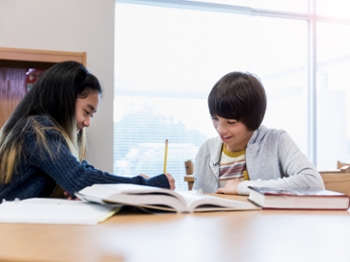 Diverse male and female middle school students work on an assignment together. They are in the school library.