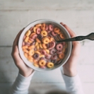 Little girl eating colorful ring-shaped cereal in a bowl of milk, seen from above, Lifestyle concept.