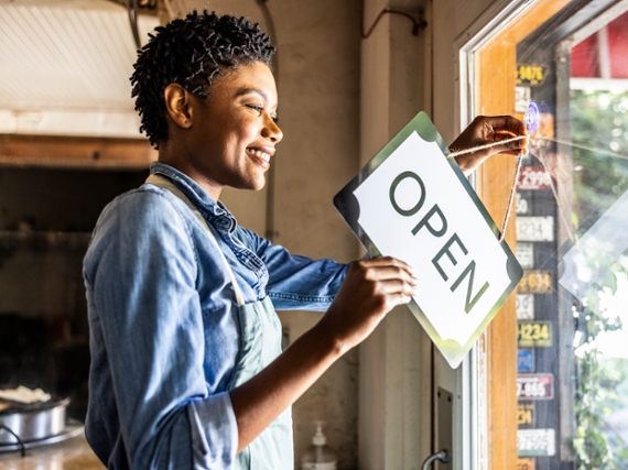 Female small business owner placing open sign in business window