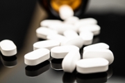 A close-up image of numerous white pills scattered from an open bottle against a dark background, symbolizing the issues of opioid abuse and the risk of drug overdoses.