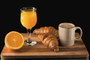 Close up of freshly made croissants surrounded by orange juice and coffee on a wooden board on a dark background. Selective focus. Breakfast concept.