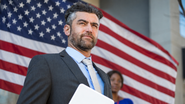 A man in a suit standing in front of an American flag