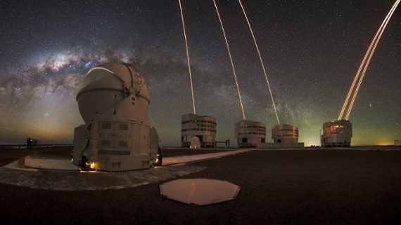 bright green lasers shoot skyward between domed telescopes under a starry night sky in the desert