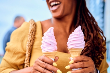 Woman holding up two pink soft serve ice creams outside  cafe