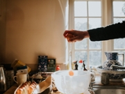 A confident male uses one hand to crack an egg open over a large plastic mixing bowl. It falls from a height.