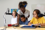 Elementary age students collaborating with their teacher while recording a podcast in a vibrant school radio studio, surrounded by technology