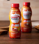 Two bottles of Premier Protein Pumpkin Spice shakes on a wooden countertop