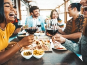 Happy friends drinking red wine sitting at restaurant table - Multiracial young people enjoying rooftop dinner party together - Food and beverage concept with guys and girls having lunch break outside