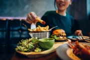 Cropped shot of young woman eating freshly made delicious burger, dipping fries in ketchup on the dining table. Enjoying a feast in the restaurant. People, food and lifestyle