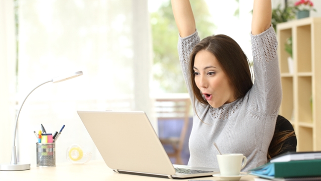 A woman cheering in front of a laptop