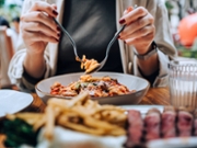 Close-up, mid-section of young Asian woman sitting at dining table holding cutleries, twirling freshly served spaghetti bolognese and enjoying her meal in restaurant. Dining out. People, food and lifestyle