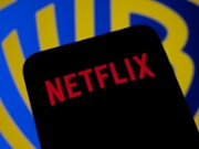 In this photo illustration, the Netflix logo appears on a cell phone with the Warner Bros. logo in the background, in Creteil, France, on December 10, 2025. (Photo by Samuel Boivin/NurPhoto via Getty Images)