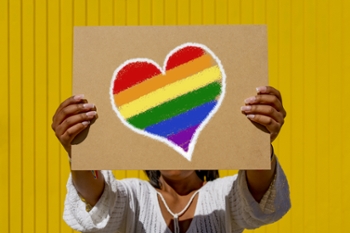 Woman holding rainbow flag heart placard sign, symbol of LGBT love during Pride Parade. Equality march to support and celebrate LGBT+, LGBTQ Gay and lesbian community.