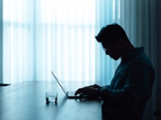 Man in dark working on laptop sitting at table. Network security. Hacker tracking. Cyber crime concept.
