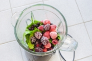 High angle photography of a jug blender full of frozen fruits and vegetable leafs ready for making a smoothie.