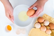 Hands breaking one egg in a ceramic bowl, with whites and yolks.