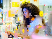 Portrait of young woman working in modern office surrounded by multicoloured social media icons and data screens. Data personalisation and social media concept.