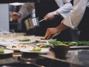 Side view of two cooks preparing vegetarian food inside their kitchen. Green lettuce served.