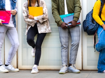 Group of multiracial teenage college students ready to go back to school standing against blue background wall. Higher education concept.