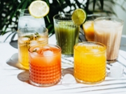 Various refreshing non-alcoholic drinks in glasses with ice. Different juice, lemonade, iced coffee, kombucha and smoothies on table and green plant background.