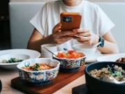 Mid-section of young Asian woman taking photos of scrumptious Chinese dishes on dining table with smartphone in restaurant. Enjoying her meal and sharing foodie photos on social media. Digital dining. People, food, lifestyle and technology