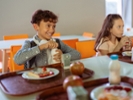 Boy opening bottle. Cheerful boy opening his bottle of milk while having lunch with classmates