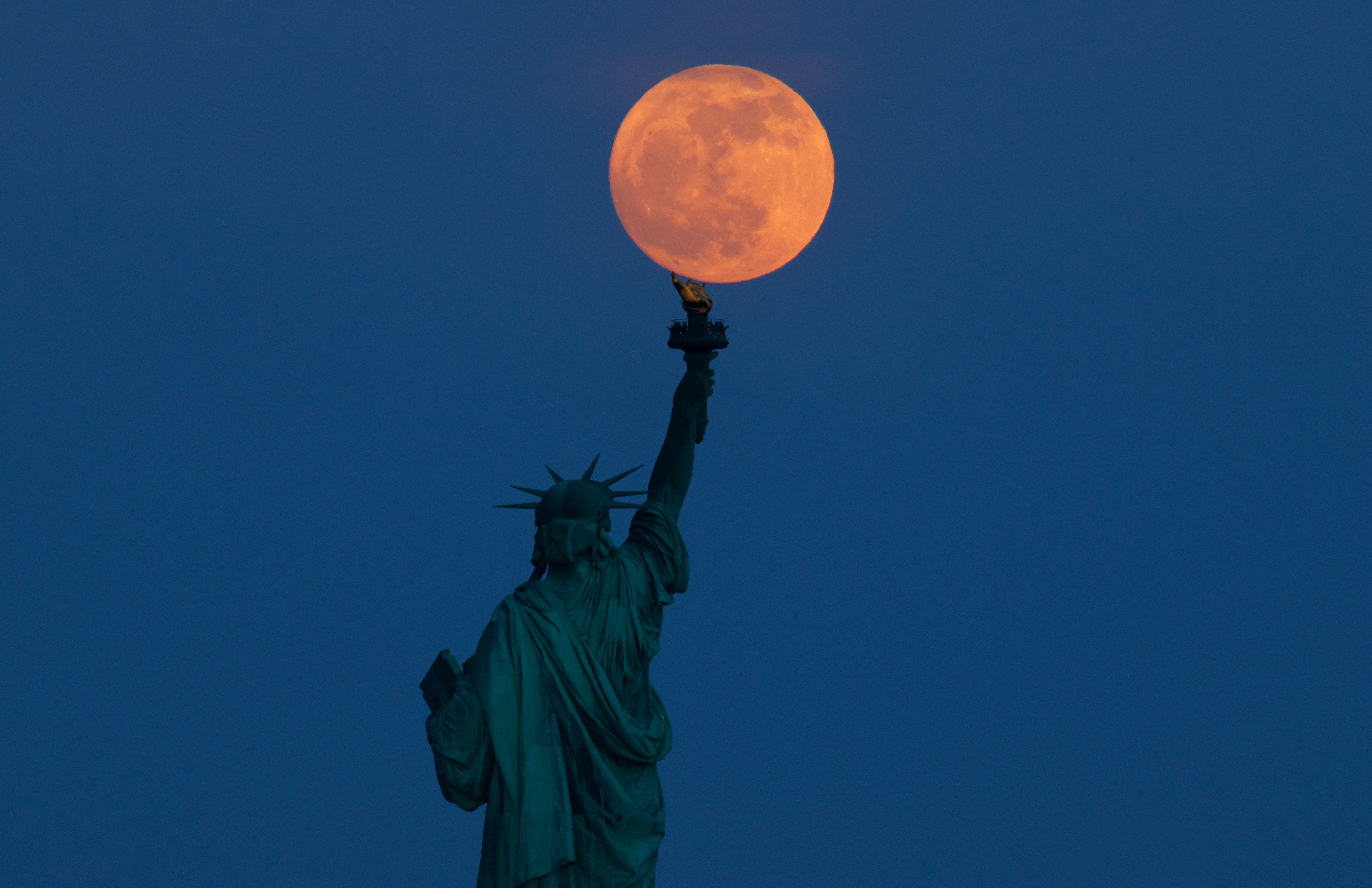 JERSEY CITY, NJ - MAY 22: The full Flower Moon rises behind the Statue of Liberty at twilight in New York City on May 22, 2024, as seen from Jersey City, New Jersey. (Photo by Gary Hershorn/Getty Images)