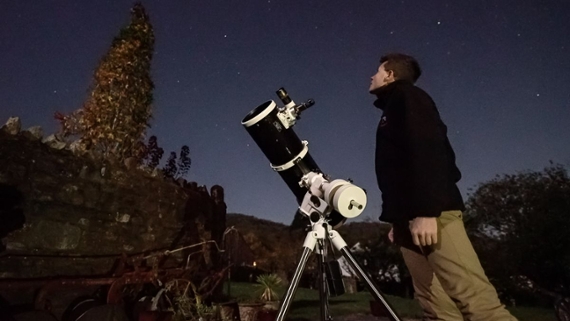 a person stands beside a telescope, staring up at the night sky