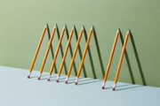 A group of pens and pencils leaning against a wall with one missing