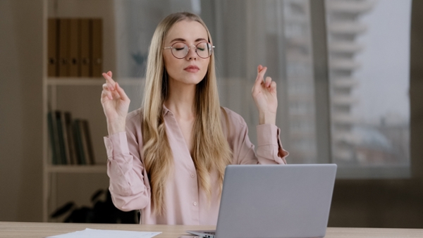 A woman sat in front of a laptop with her fingers crossed