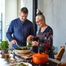 Woman in her 60s making fresh salad in bowl with help from male friend, togetherness, support, healthy lifestyles