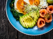 Smoked salmon with sunny side up eggs, avocado and leafy vegetables on wooden table