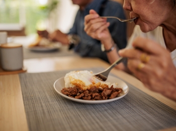 Mature Thai man and woman share a pleasant lunch together at the dining table in their home.