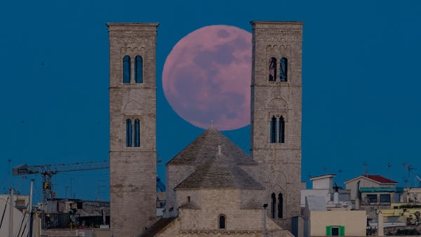 A red full moon is pictured rising between two stone towers that loom over the rooftops of a town in Italy.