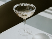 Single glass of Margarita cocktail with a rim of salt sitting on a shadowy table with space for copy.