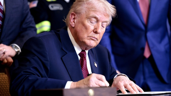 Donald Trump sitting at a desk signing documents