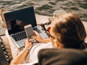 High angle view of woman with laptop text messaging on smart phone while sitting at jetty