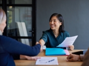 Smiling chinese candidate shakes hands during a job interview with female boss. Professional interview with candidate presenting documents. Financial advisor shaking hands after meeting a couple interested in new investments.