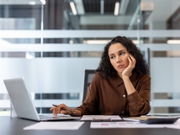 Stressed businesswoman at modern office desk with laptop, exhausted and unmotivated, slumped in thought from long hours and burnout, looking tired and disconnected