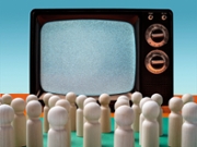Many little wooden figures facing large vintage television set on green surface, blue background