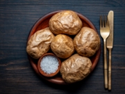 Simple baked potatoes whole in their skins and salt in clay plate on wooden table, close up, top view