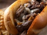 Closeup of philly cheesesteak sandwich made with steak, cheese and onions on a toasted hoagie roll with french fries on a wooden table