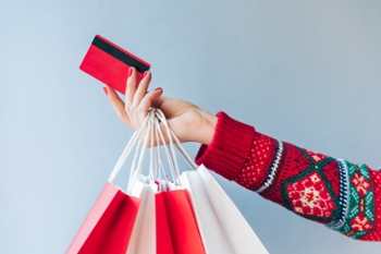 Close up crooped shot of woman hand holding many paper handbags and red credit card. Holiday shopping, black friday sales concept.