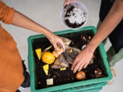 Young woman and her younger brother making compost from kitchen food leftovers into rich organic soil fertilizer.