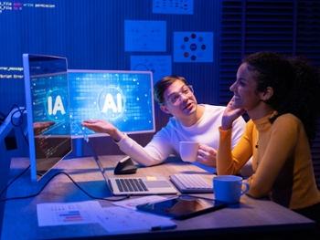 Two young colleagues discuss AI technology at night, pointing at glowing computer monitors displaying artificial intelligence interface.