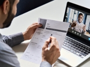 Male indian hr, recruiter or employer holding cv having online virtual job interview meeting with african candidate on video call. Distance remote recruitment conference chat. Over shoulder view.