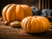 Front view of two whole pumpkins with some pumpkin seeds on a rustic wooden table