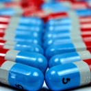 Tylenol capsules lying on a counter. Capsules are arranged in rows in the foreground. The background shows a disorganized pile of capsules. The capsules are red, white, and blue Tylenol pills.