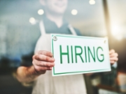 Cropped shot of an unrecognizable male coffee shop owner hanging a "HIRING" sign in his window