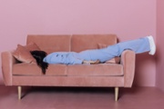 A woman in a blue suit lies on a pink sofa.